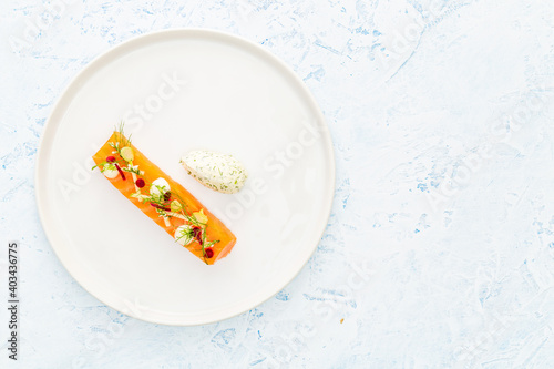 Raw salmon with apple, edible flowers, zucchini and beetroot on a white and blue plate aside silver cutlery and a quenelle of cheese with dill over a blue background with copy space.