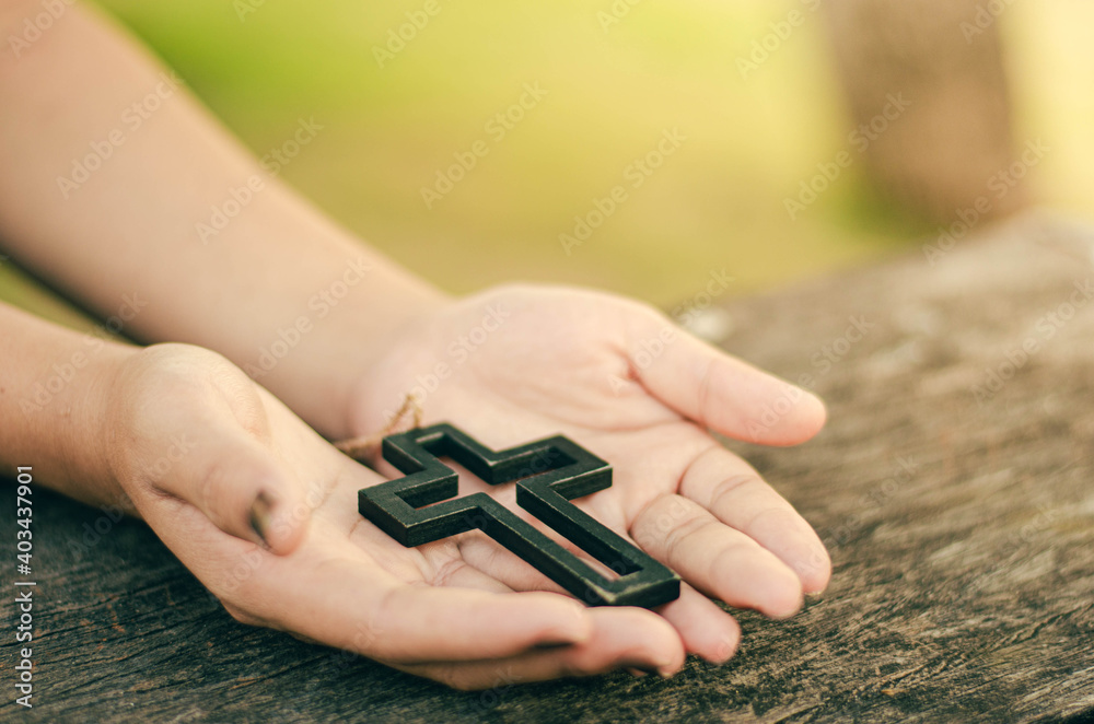 Image of young woman hand holding and raising crucifix christian religious symbols in light and scenery religious background faith concept