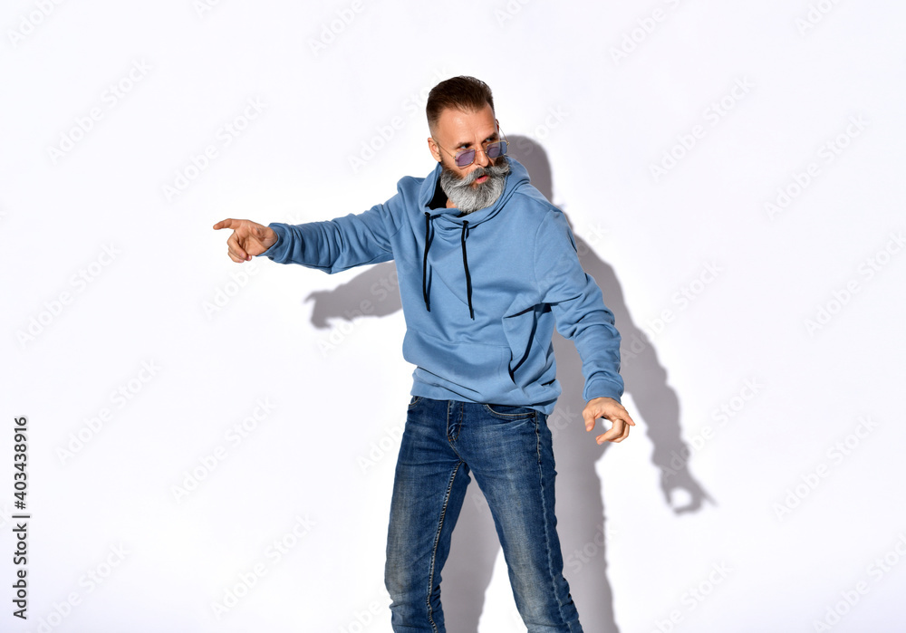 Frowning bearded man wearing trendy sunglasses, casual sweatshirt, fashion jeans denim standing looking aside in motion. Studio shot isolated on white background Frowning bearded man wearing trendy sunglasses, casual sweatshirt, fashion jeans denim standing looking aside in motion. Studio shot isolated on white background