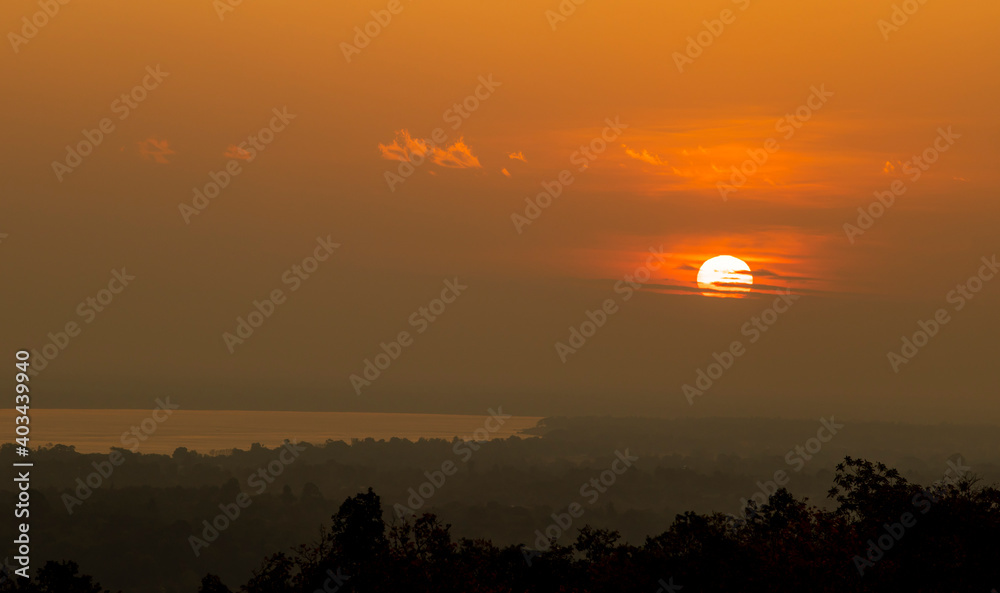 Landscape with a deep morning dawn with highlights in the orange rays of the summer sun on the river against a grove of trees with highlights of light