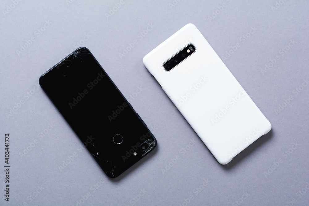 Old broken black and new white smartphones on gray background. The concept of recycling phones and technologies. Old broken black and new white smartphones on gray background. The concept of recycling phones and technologies.