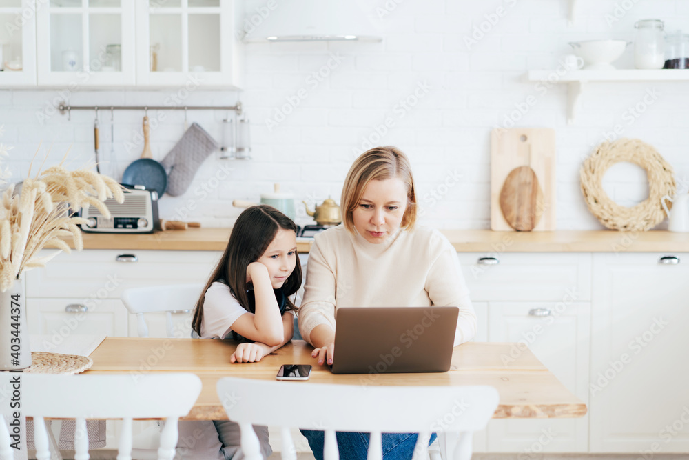 Mom and daughter at the table in the kitchen with a laptop work, study and communicate online. Mom and daughter at the table in the kitchen with a laptop work, study and communicate online.