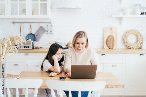 Mom and daughter at the table in the kitchen with a laptop work, study and communicate online.