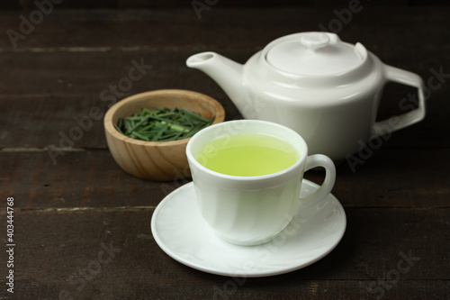 Lemon grass tea in white cup and lemon grass leaf in wooden bowl with white teapot on wooden background. Healthy herbal drink concept.