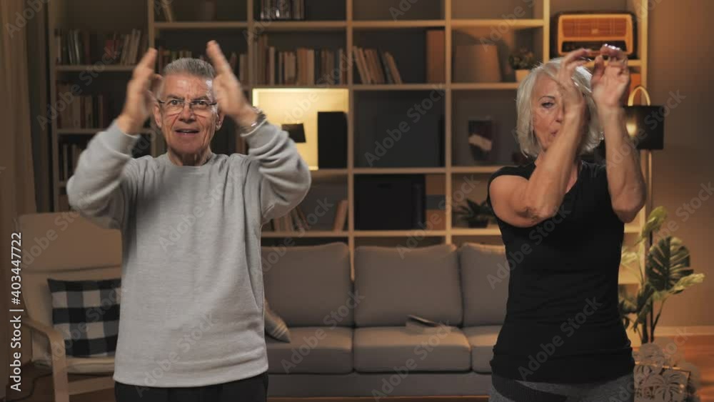 old senior couple exercise at home looking at the camera,active healthy lifestyle,caucasian elderly man and woman workout together in living room front view