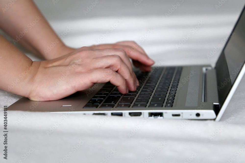Female hands on laptop keyboard on a bed. Woman working at a ultrabook at home, remote work Female hands on laptop keyboard on a bed. Woman working at a ultrabook at home, remote work