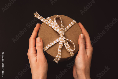 Colorful gift with beige rope in woman's hands on a dark background