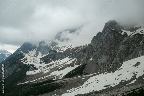 A panoramic view on the Alpine peaks in Austria from Marstein. The slopes are mostly covered with snow. Stony and sharp mountains. Overcast. Baren slopes, green valley below. Serenity and calmness photo