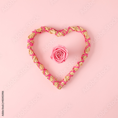 Heart shape frame made of straw with pink rose in center. Valentine's day flat lay concept.