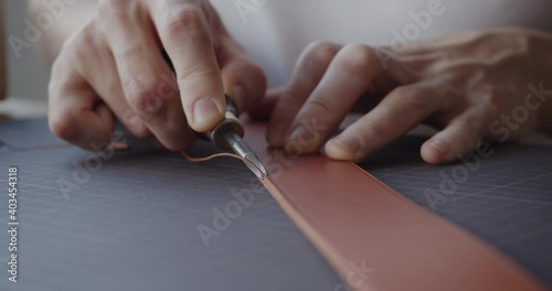Making handmade leather belt. Young leather worker using leather edge beveler during belt manufacturing process in his workshop. Close-up shot.