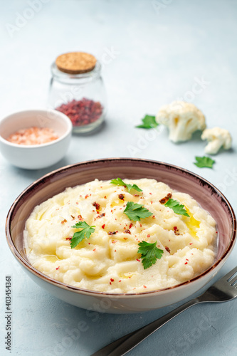 Mashed cauliflower with butter, pink peppercorns and parsley on concrete background