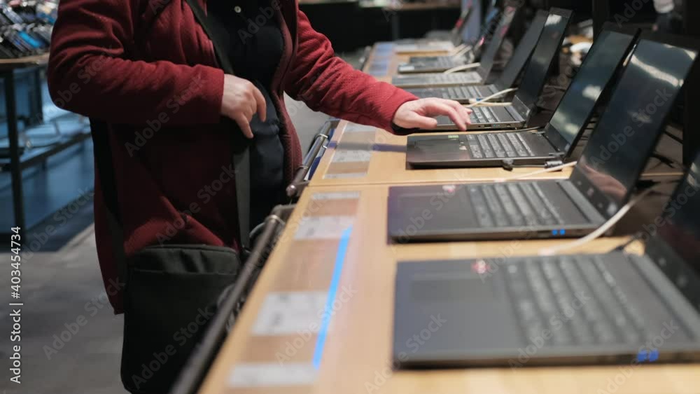 Rows of laptops in the store of devices and gadgets. The girl buys herself a new laptop computer. Carefully examines the product, presses the keyboard
