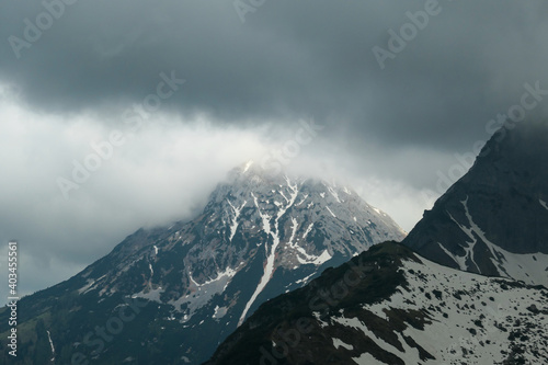 A panoramic view on the Alpine peaks in Austria from Marstein. The slopes are mostly covered with snow. Stony and sharp mountains. Overcast. Baren slopes, green valley below. Serenity and calmness