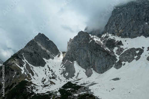 A panoramic view on the Alpine peaks in Austria from Marstein. The slopes are mostly covered with snow. Stony and sharp mountains. Overcast. Baren slopes, green valley below. Serenity and calmness photo