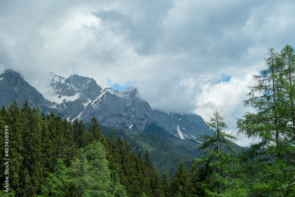 A panoramic view on the Alpine peaks in Austria from the Marstein. The slopes are still partially covered with snow. Stony and sharp mountains. Overcast. Baren slopes, dense forest at the foothill.