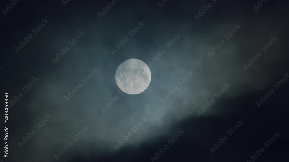 Bright white moon behind dark clouds moving in the night sky - Close up Bright white moon behind dark clouds moving in the night sky - Close up