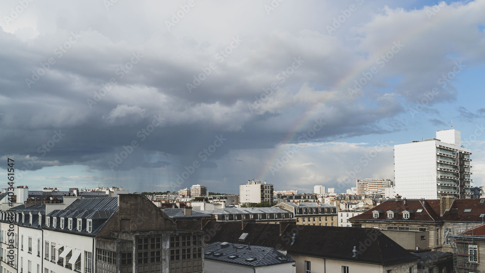 Panorama sur les toits de paris, un arc-en-ciel traverse le ciel, des nuages sombres, il pleut.