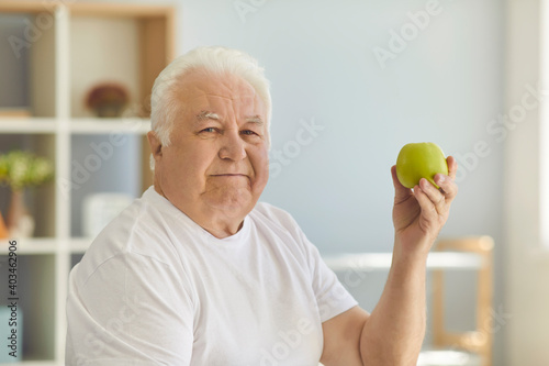 Senior man holding green apple and recommending eating raw fruit and keeping healthy diet