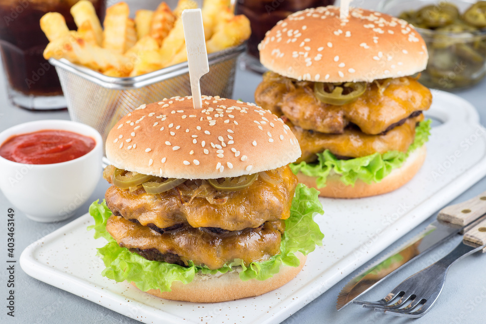 Double cheese burger with caramelized onion, lettuce and jalapeno, served with french fries and soda, on white plate, horizontal Double cheese burger with caramelized onion, lettuce and jalapeno, served with french fries and soda, on white plate, horizontal