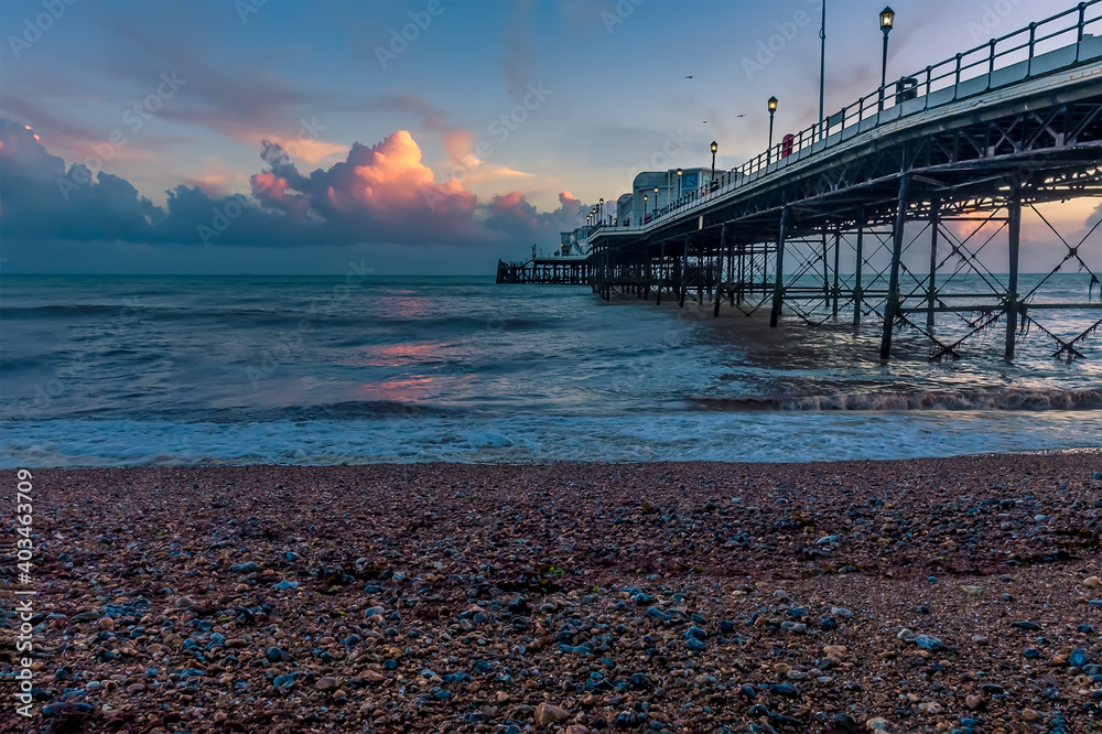 The receding sun casts a pink glow over the sea next to the pier at Worthing, Sussex, UK