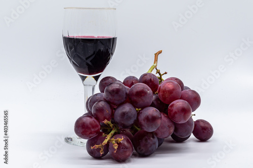 Glass of red wine with bunch of red grapes on white background