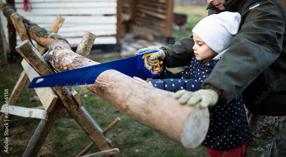 Obscured man in military uniform teaching little girl how to saw firewood in yard of cottage in winter