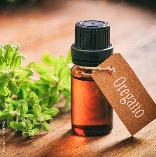 Oregano essential oil and fresh leaves on wooden background