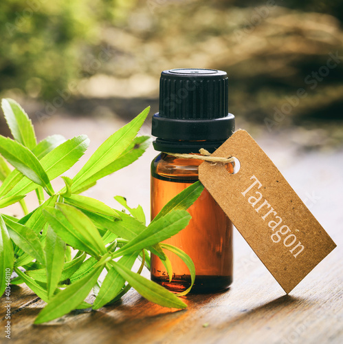 Fresh tarragon plant leaves and essential oil on wooden background.