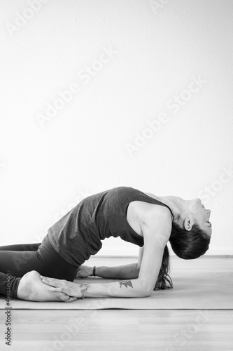 Black and white vertical view of a brunette young woman practicing yoga indoors in her home interior, doing a backbend asana variation.