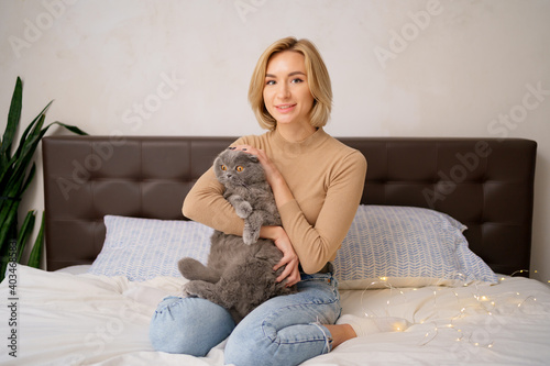 Pets, morning, comfort, rest and people concept - happy young woman with cat in bed at home