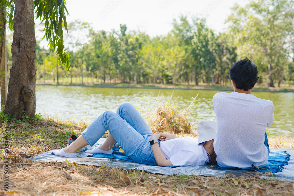 asian couple picnic and relax with happiness feeling in park with lake in springtime