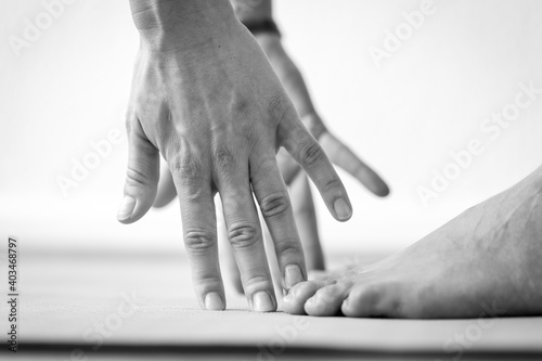 Close-up side view of the hands and feet of a young woman on the way to the Uttanasana or Standing Forward Bend yoga pose. © Dante