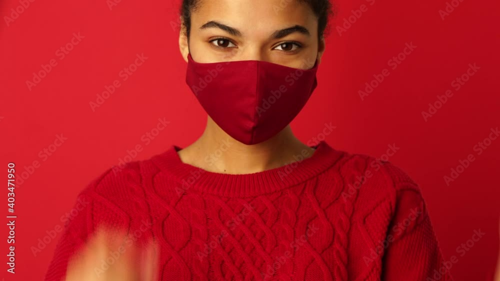 Be protected. Young mixed race girl putting on protective face mask and then taking it off, smiling at camera isolated over red background. Safety, coronavirus concept Be protected. Young mixed race girl putting on protective face mask and then taking it off, smiling at camera isolated over red background. Safety, coronavirus concept