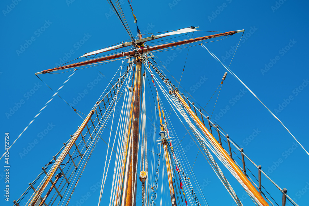 Old sailing ship wood mast, rigging of a sailing ship detail against blue sky Old sailing ship wood mast, rigging of a sailing ship detail against blue sky