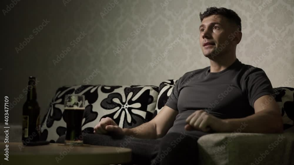 A man cheerleader is watching a sports match on the sofa at home. The soccer fan cheers for his team in the interior. Viewing sports events A man cheerleader is watching a sports match on the sofa at home. The soccer fan cheers for his team in the interior. Viewing sports events