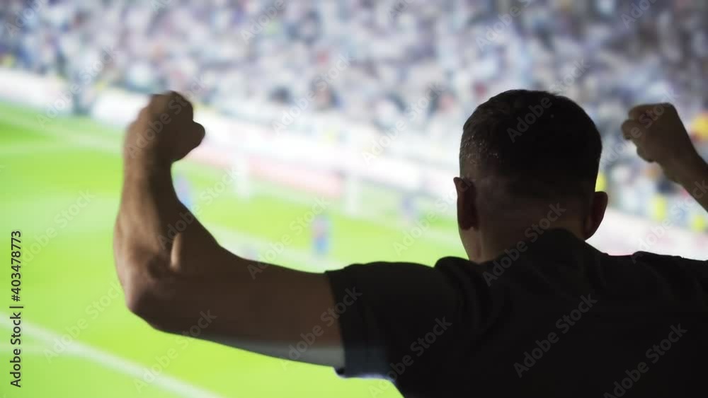 A man cheerleader is watching a sports match on the background of the screen. The soccer fan cheers for his team in the interior. Viewing sports events