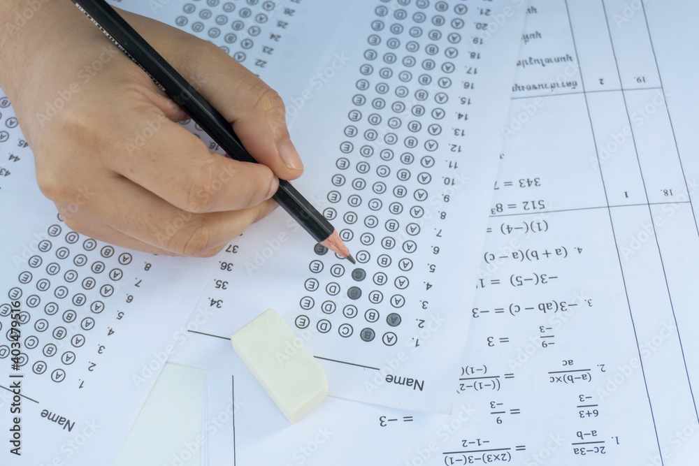 Students hand holding pencil writing selected choice on answer sheets and Mathematics question sheets. students testing doing examination. school exam Students hand holding pencil writing selected choice on answer sheets and Mathematics question sheets. students testing doing examination. school exam