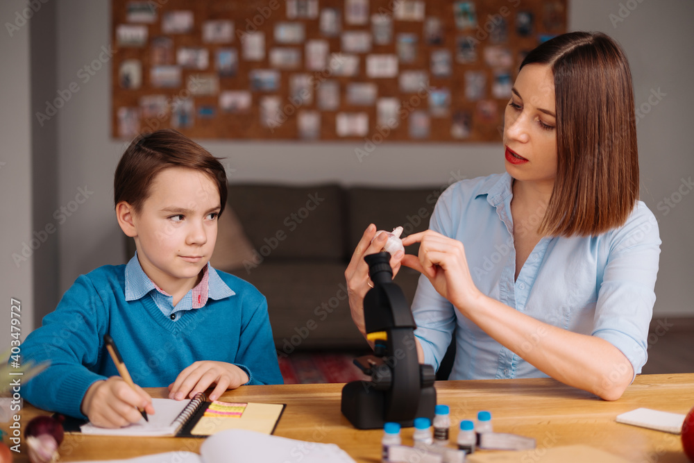 Fototapeta premium Aunt and nephew do homework together. Women explain kid writes in notebook. Schoolboy studying at home. Family relationships, primary education, childhood