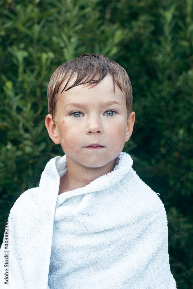 Little boy wrapped in a towel after bathing outdoors.