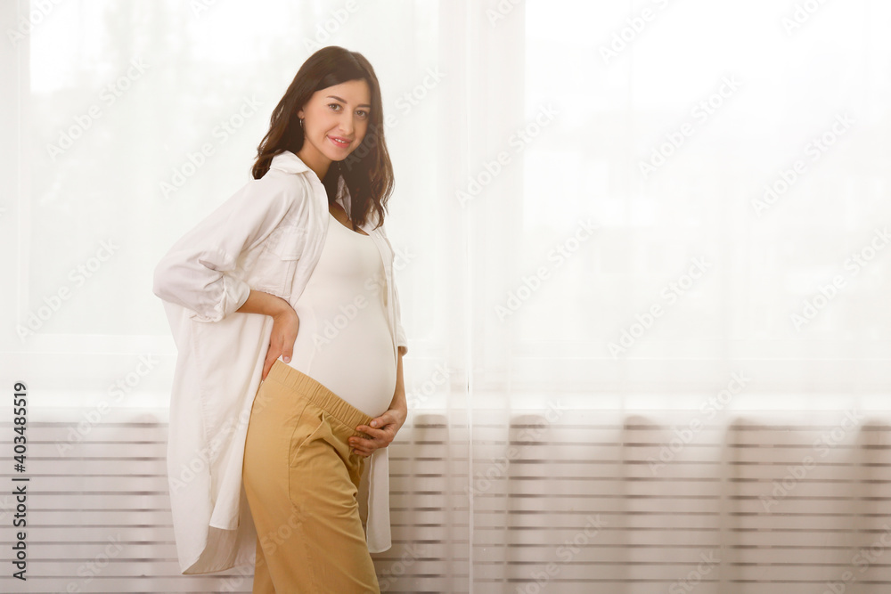Portrait shot of young beautiful woman on second trimester of pregnancy. Close up of pregnant female in casual attire with arms on her round belly. Expecting a child concept. Background, copy space. Portrait shot of young beautiful woman on second trimester of pregnancy. Close up of pregnant female in casual attire with arms on her round belly. Expecting a child concept. Background, copy space.