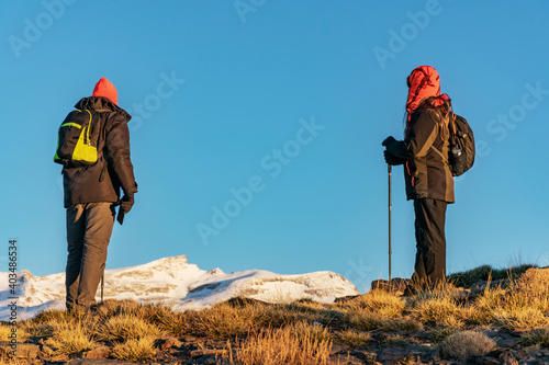 Two hikers contemplating the landscape of the Sierra Nevada mountains with snow.
