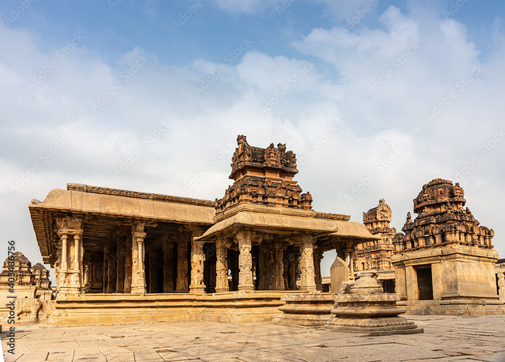 Hampi, Karnataka, India - November 5, 2013: Sri Krishna temple in ruins. 3 Brown-stone Vimanams on small shrine and larger ones on sanctums under blue cloudscape.