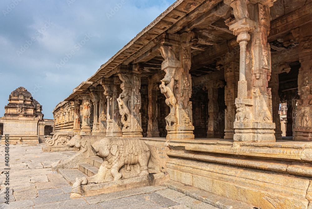 Hampi, Karnataka, India - November 5, 2013: Sri Krishna temple in ruins. brown stone intensively carved sculpted pillars and balusters along mandapam hall under blue sky.