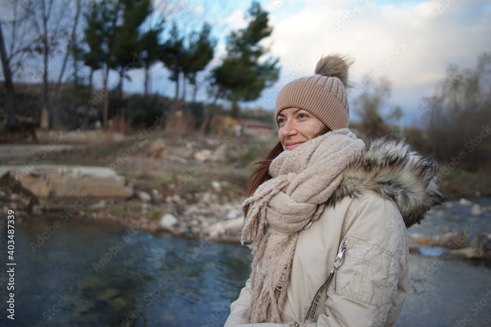 Chica caucásica morena con gorro junto a un rio en un atardecer de invierno Chica caucásica morena con gorro junto a un rio en un atardecer de invierno