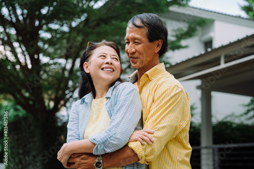 Asian senior couple hugging outdoors in backyard.