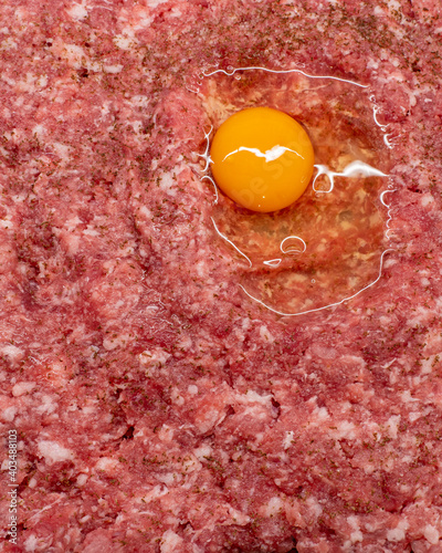 Surowe mielone mięso wieprzowe a na nim rozbite jajko. Wszystko przyprawione solą i pieprzem. 