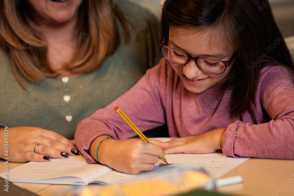 Mother helps her daughter with homework sitting at the living room table at home. Mother helps her daughter with homework sitting at the living room table at home.