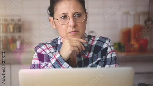 Serious worried mature woman working at home on a laptop thinking about how to solve a problem. Portrait of a thoughtful lady with glasses.