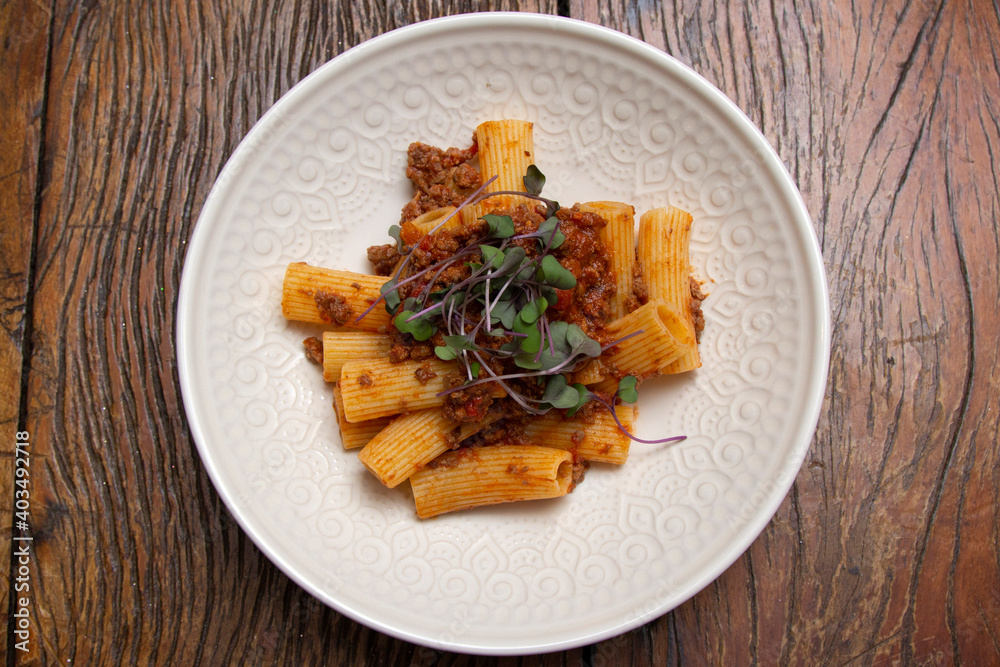 Rigatoni pasta with sugo sauce and lamb ragout, with coriander leaves on top.