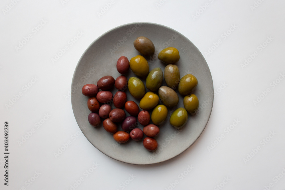 Green and purple olives on grey concrete plate isolated on white background from a high angle view Green and purple olives on grey concrete plate isolated on white background from a high angle view